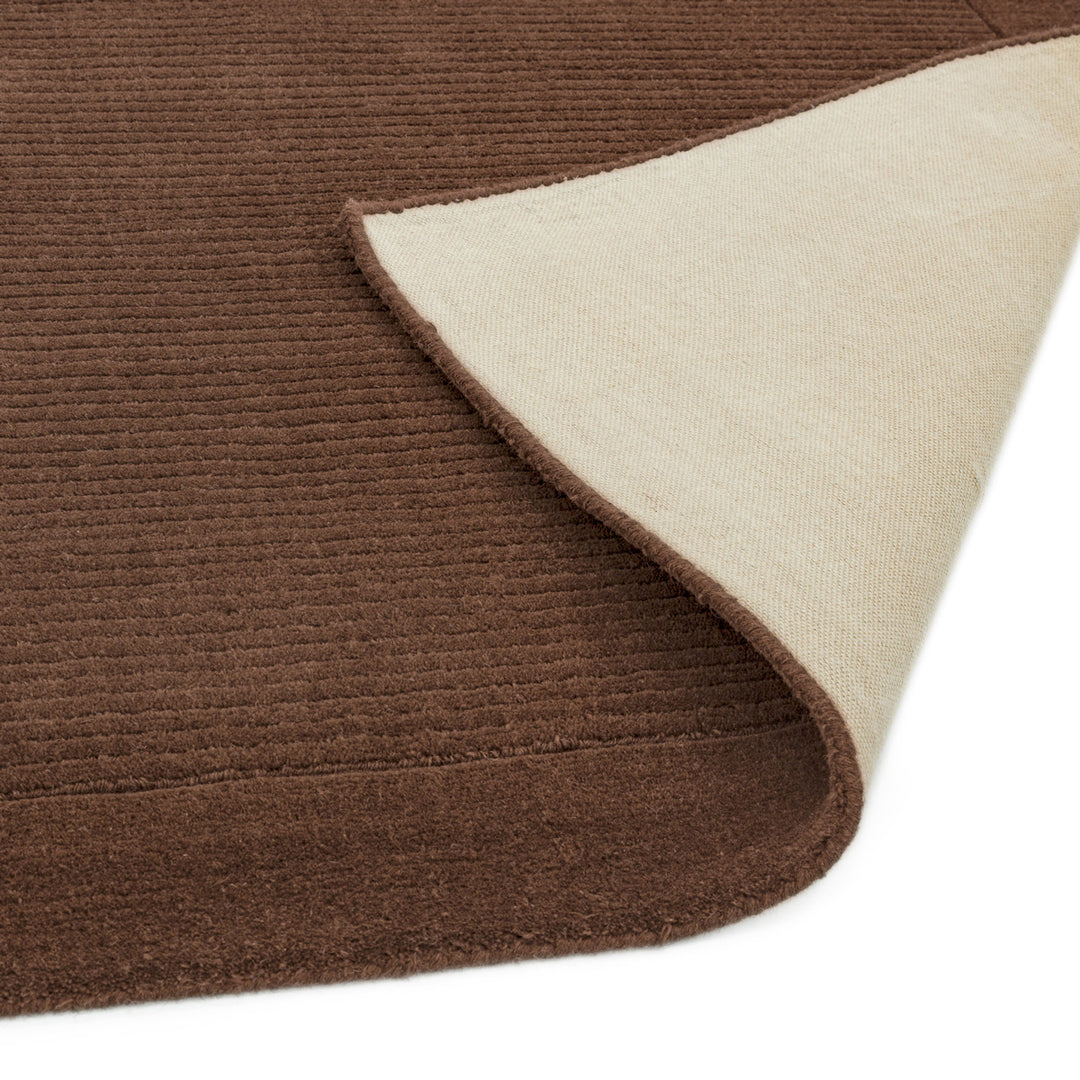 暖色アーシーカラーの落ち着いたチョコレートブラウン色に、リブとボーダーがスタイリッシュ感を添える、サステナブルな天然素材ウール(羊毛)100%製RUGHAUSのふんわりシンプル手織りラグの素材感と裏地がわかるクロースアップ