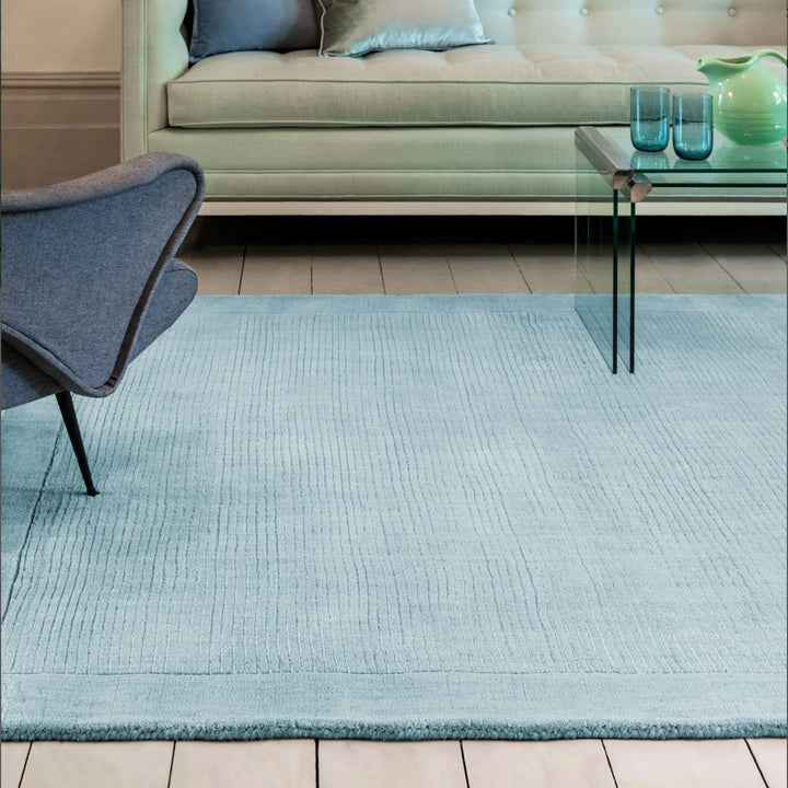 澄み渡った空を想わせる淡いベビーブルー色に、リブとボーダーがスタイリッシュ感を添える、サステナブルな天然素材ウール(羊毛)100%製RUGHAUSのふんわりシンプル手織りラグを主役にしたブルーでまとめたモダンなリビングルーム