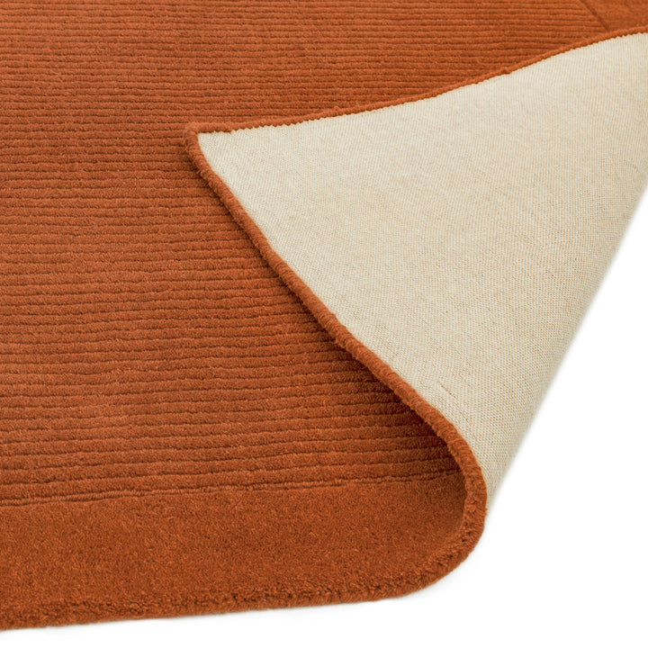 明るく温かな印象の暖色が心地よいアーシーカラー、テラコッタ(赤茶色)色の、サステナブルな天然素材ウール(羊毛)100%製RUGHAUSのふんわりシンプル手織りラグの素材感と裏地がわかるクロースアップ
