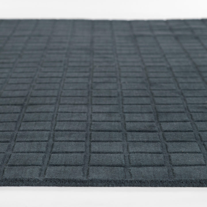 ミッドナイトブルーのように深く落ち着いた色合いのネイビーカラーとタイル模様が素敵な、RUGHAUSの天然素材ウール100％製手織りのエレガントモダンラグの素材感がわかるクロースアップ