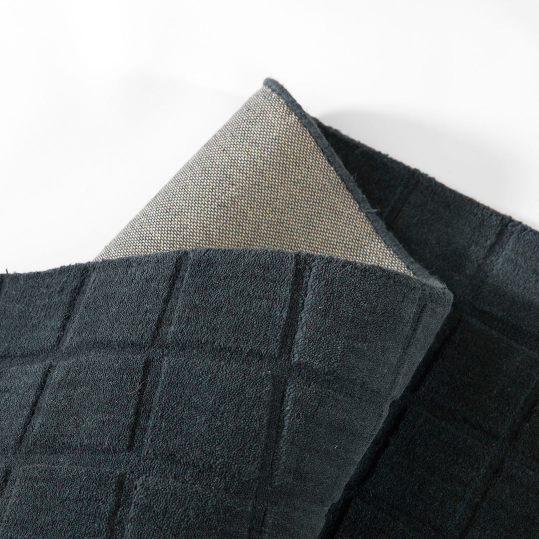 ミッドナイトブルーのように深く落ち着いた色合いのネイビーカラーとタイル模様が素敵な、RUGHAUSの天然素材ウール100％製手織りのエレガントモダンラグの素材感がわかるクロースアップ