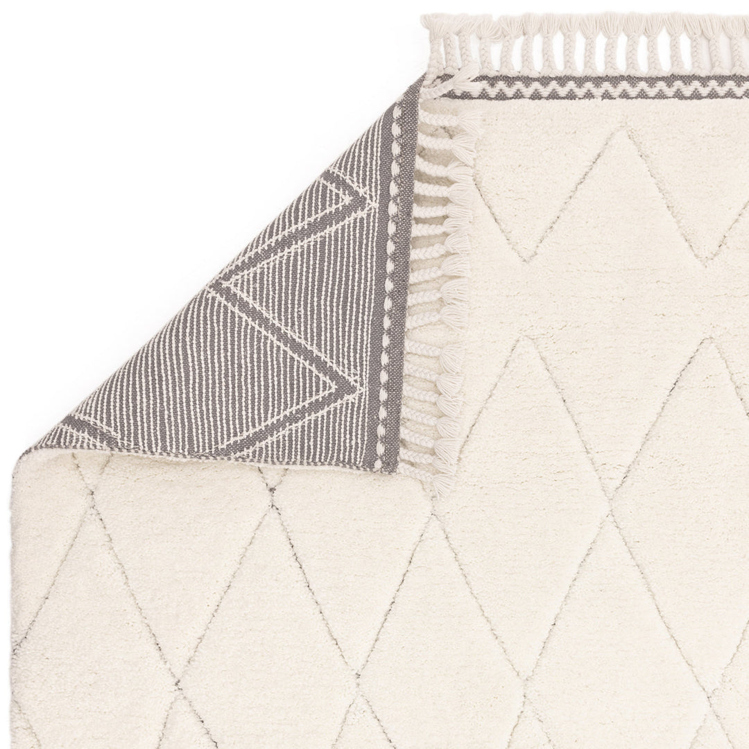 伝統的なベルベルキリムのテクスチャーやデザインにインスパイアされて織り上げた、ダイヤ模様がチャーミングな、ふわふわとした柔らかなマイクロファイバーポリエステル製RUGHAUSのベージュ・アイボリー色のベニワレンスタイルモロッカンシャギーラグの素材感と裏地がわかるクロースアップ