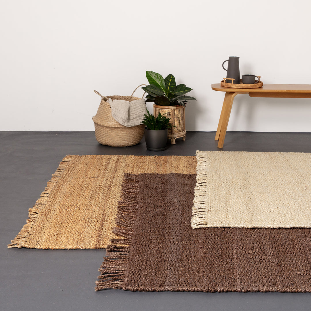 落ち着いたアーシーカラー、ブラウンの色合いとざっくりとしたナチュラルな風合いが素敵なRUGHAUSの手織りリバーシブル仕様天然エコ素材ジュート製ラグを主役にしたレイヤードラグスタイルのリビングルームイメージ