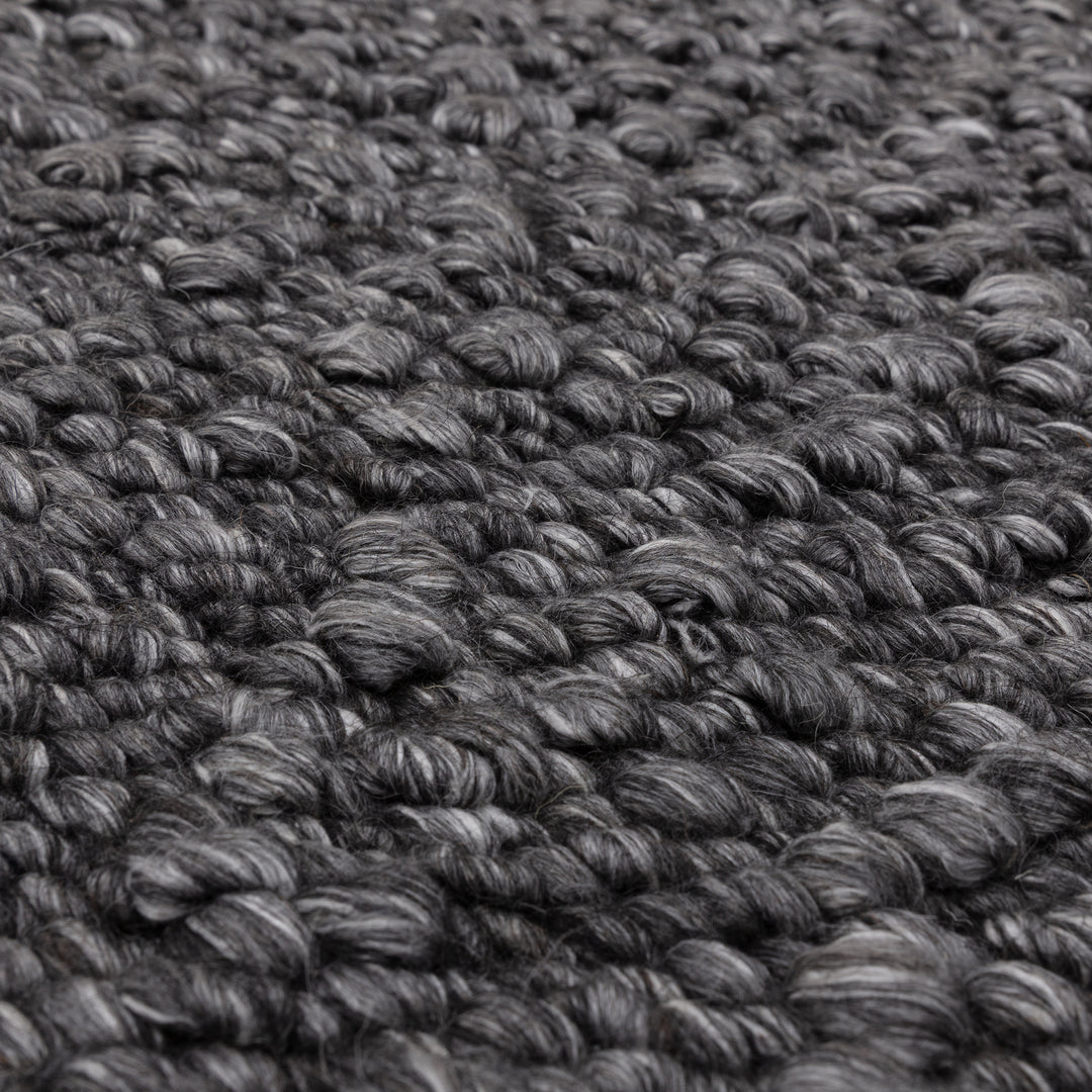 シックなチャコールグレーの色合いと、ブークレ（Boucle）織りのざっくりとした風合いがパーフェクトにマッチした、RUGHAUSの手織りのシンプルモダンラグの素材感がわかるクロースアップ