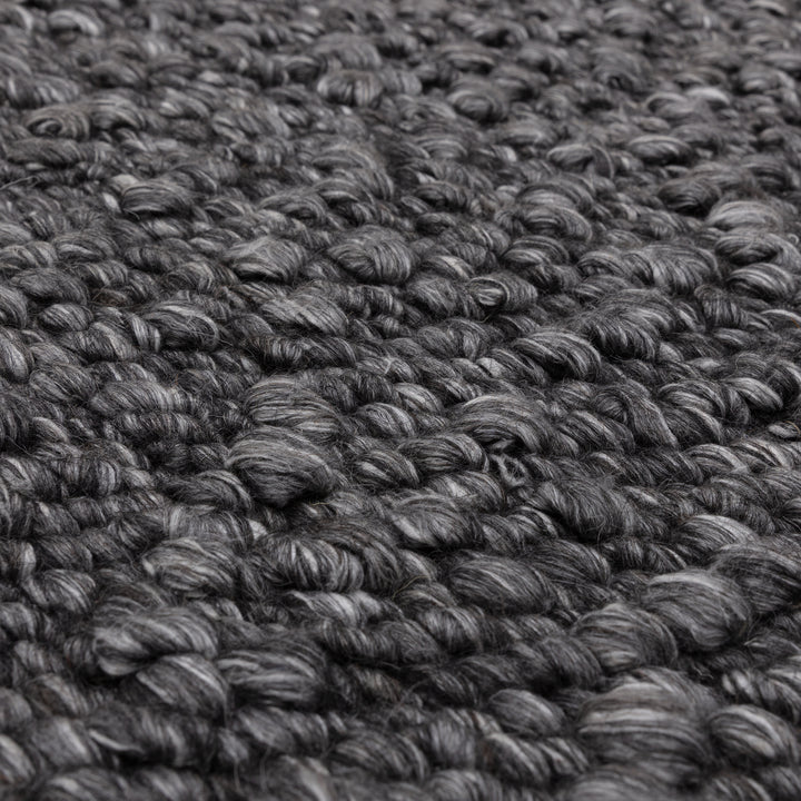 シックなチャコールグレーの色合いと、ブークレ（Boucle）織りのざっくりとした風合いがパーフェクトにマッチした、RUGHAUSの手織りのシンプルモダンラグの素材感がわかるクロースアップ