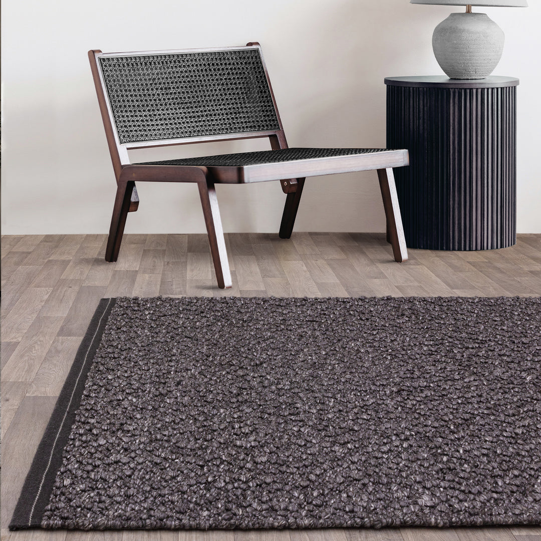 シックなチャコールグレーの色合いと、ブークレ（Boucle）織りのざっくりとした風合いがパーフェクトにマッチした、RUGHAUSの手織りのシンプルモダンラグとチェアを主役にしたアーバンなリビングルームイメージ