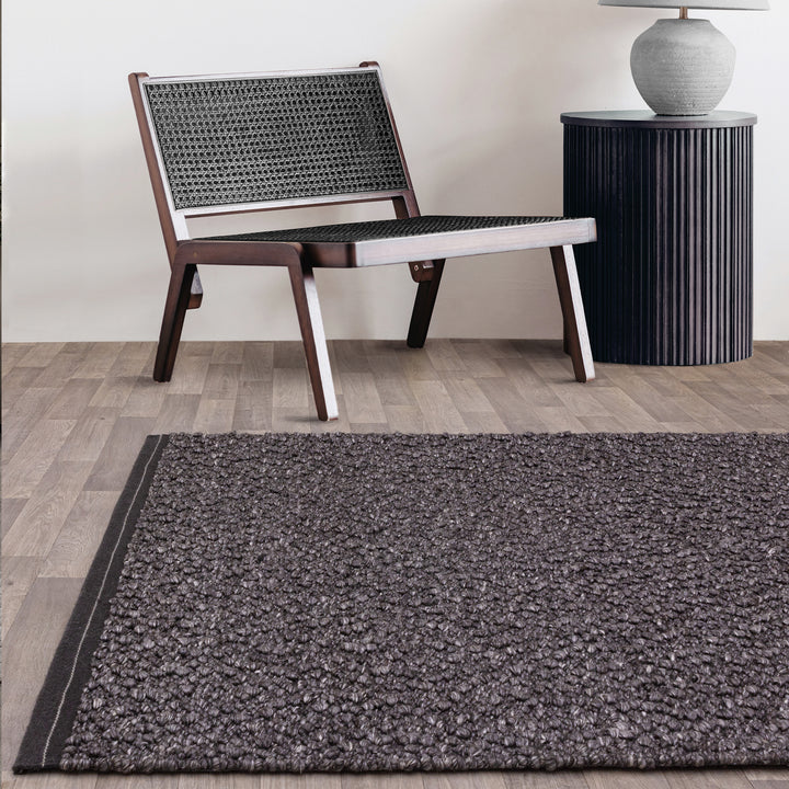 シックなチャコールグレーの色合いと、ブークレ（Boucle）織りのざっくりとした風合いがパーフェクトにマッチした、RUGHAUSの手織りのシンプルモダンラグとチェアを主役にしたアーバンなリビングルームイメージ