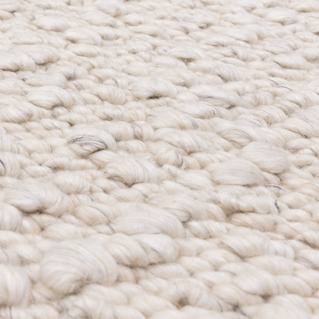 アイボリーの優しい色合いと、ブークレ（Boucle）織りのざっくりとした風合いがパーフェクトにマッチした、RUGHAUSの手織りのシンプルモダンラグの素材感がわかるクロースアップ