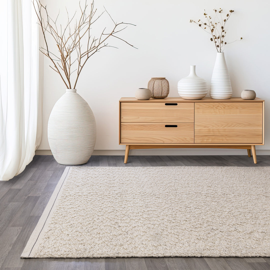 アイボリーの優しい色合いと、ブークレ（Boucle）織りのざっくりとした風合いがパーフェクトにマッチした、RUGHAUSの手織りのシンプルモダンラグを主役にした北欧スタイルのリビングルームイメージ