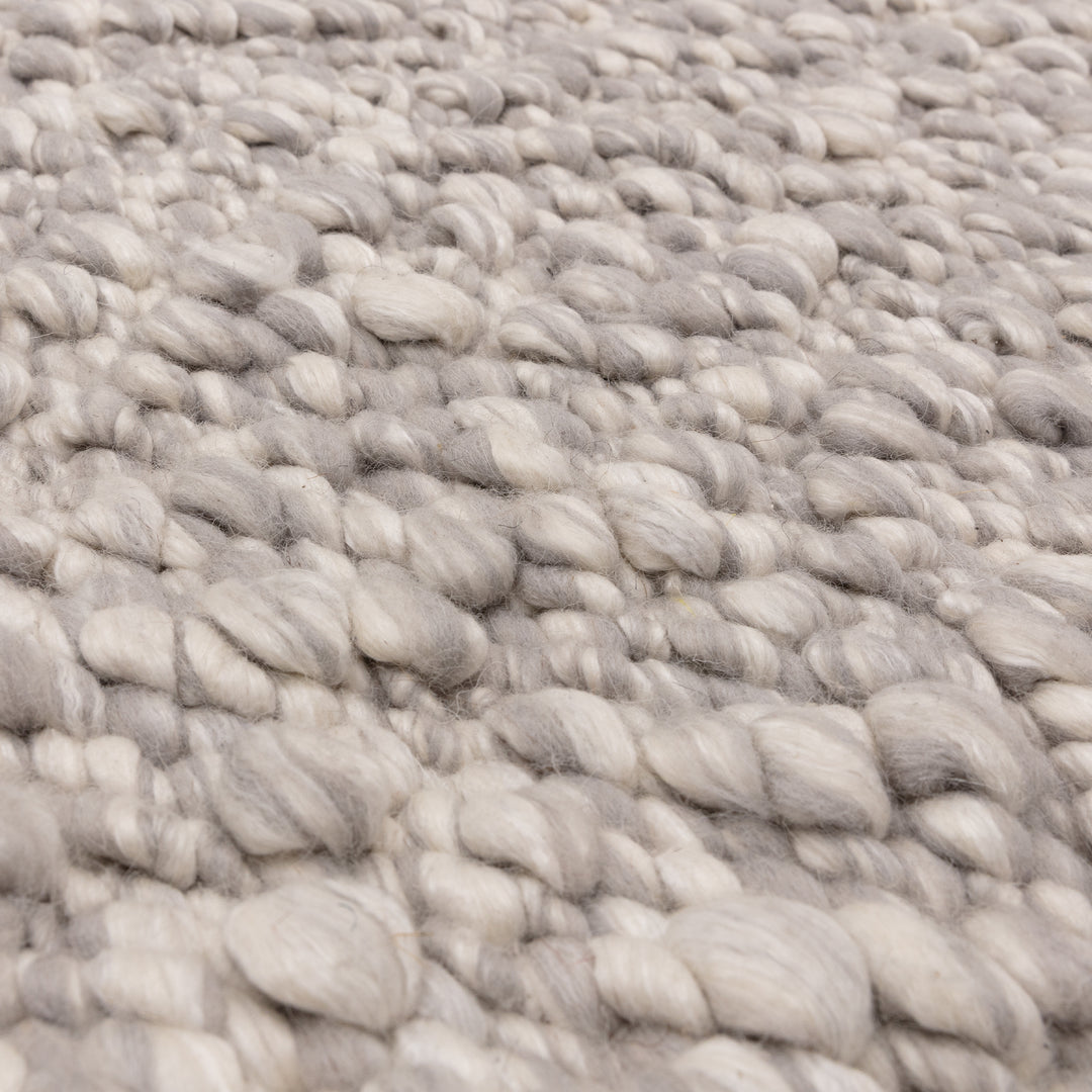 洗練されたライトグレーの色合いと、ブークレ（Boucle）織りのざっくりとした風合いがパーフェクトにマッチした、RUGHAUSの手織りのシンプルモダンラグの素材感がわかるクロースアップ