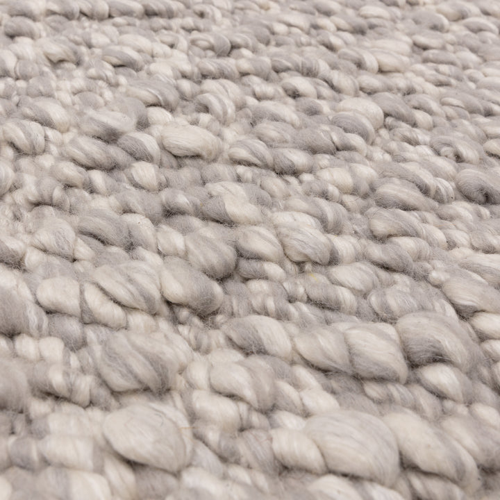 洗練されたライトグレーの色合いと、ブークレ（Boucle）織りのざっくりとした風合いがパーフェクトにマッチした、RUGHAUSの手織りのシンプルモダンラグの素材感がわかるクロースアップ